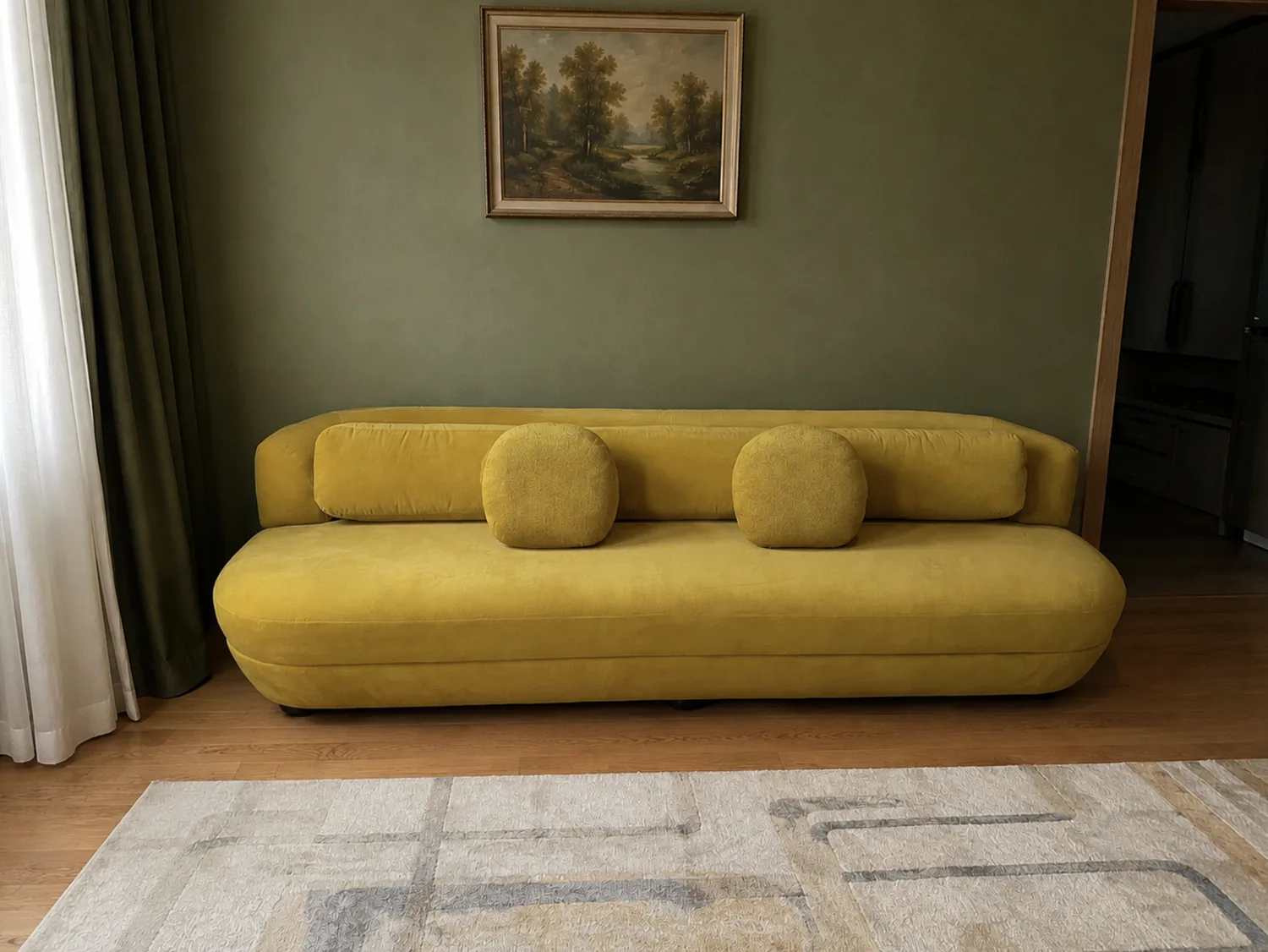 Low mustard velvet sofa with two bolsters against a green wall