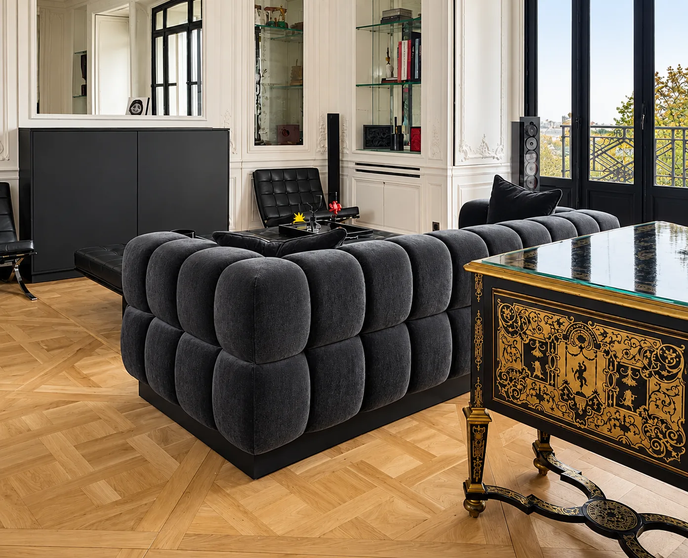 A channel-tufted charcoal sofa beside an inlaid antique desk on parquet