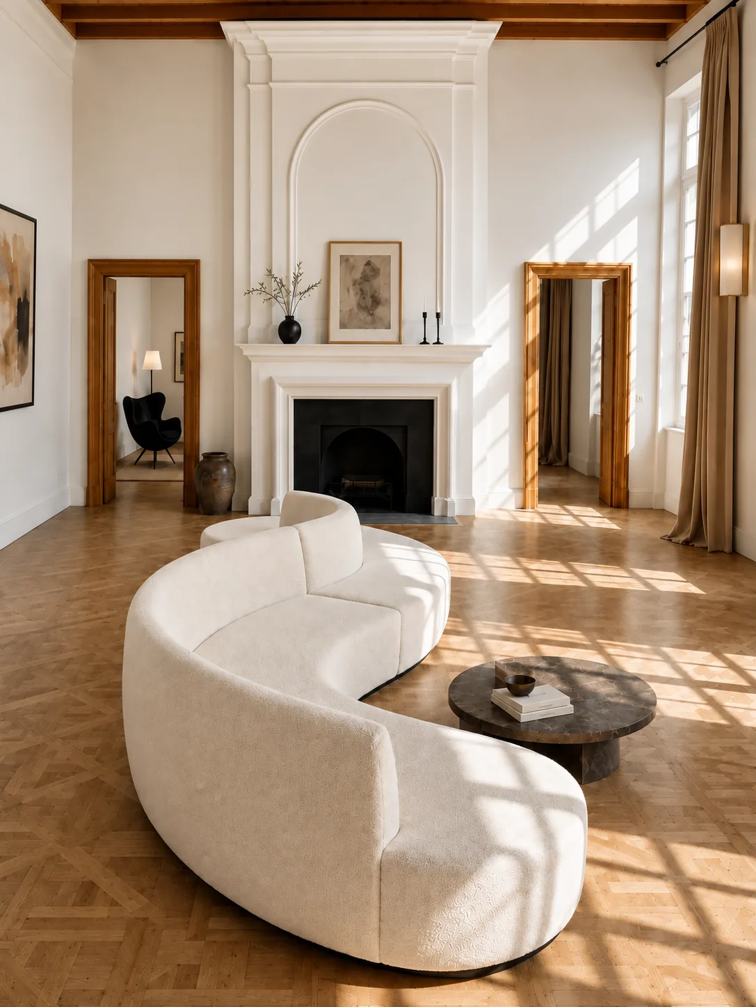 A curved cream sofa before a white marble fireplace in a sunlit room