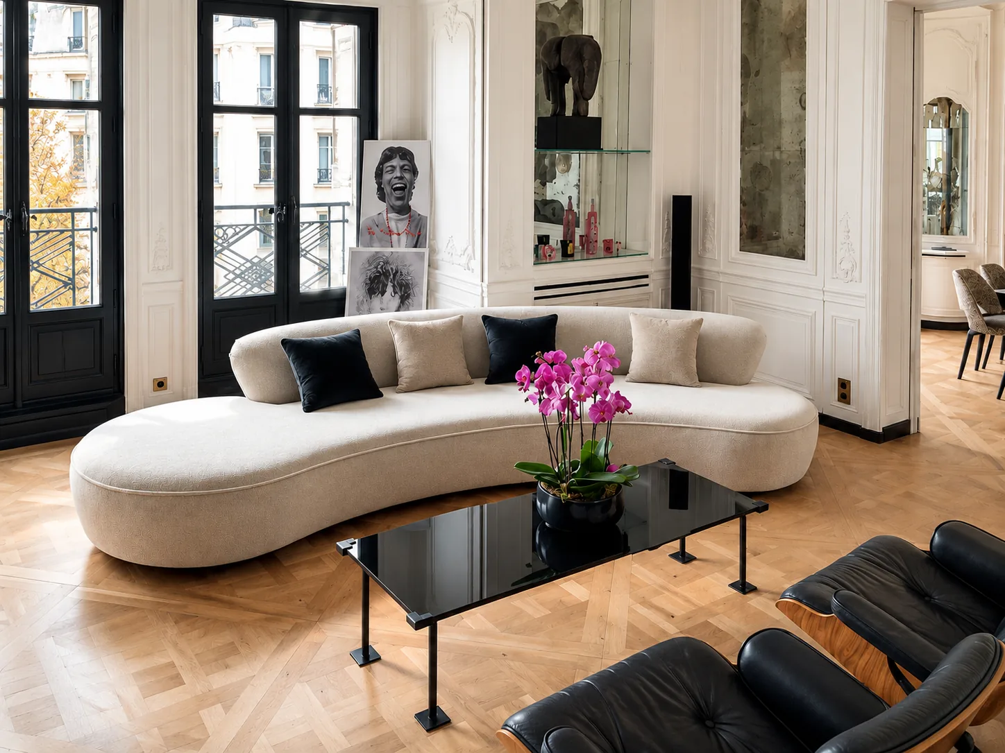 A curved cream sofa with dark cushions and a black glass coffee table in a panelled Parisian salon