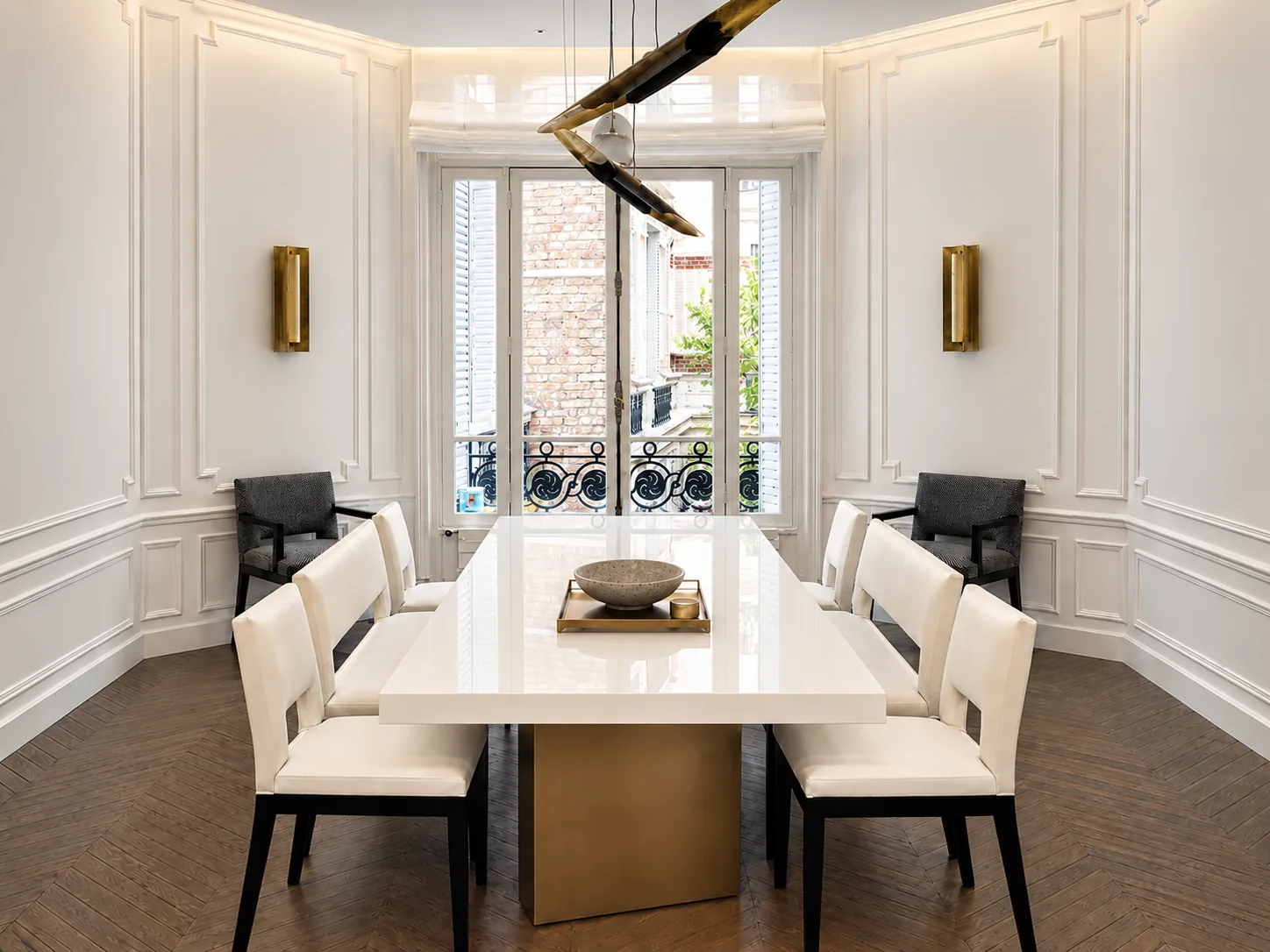 A white lacquer dining table on a brass base with cream upholstered chairs, in a panelled dining room