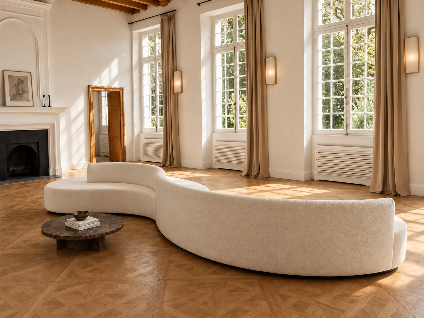 A long serpentine cream sofa and a low stone table in a bright room with tall windows