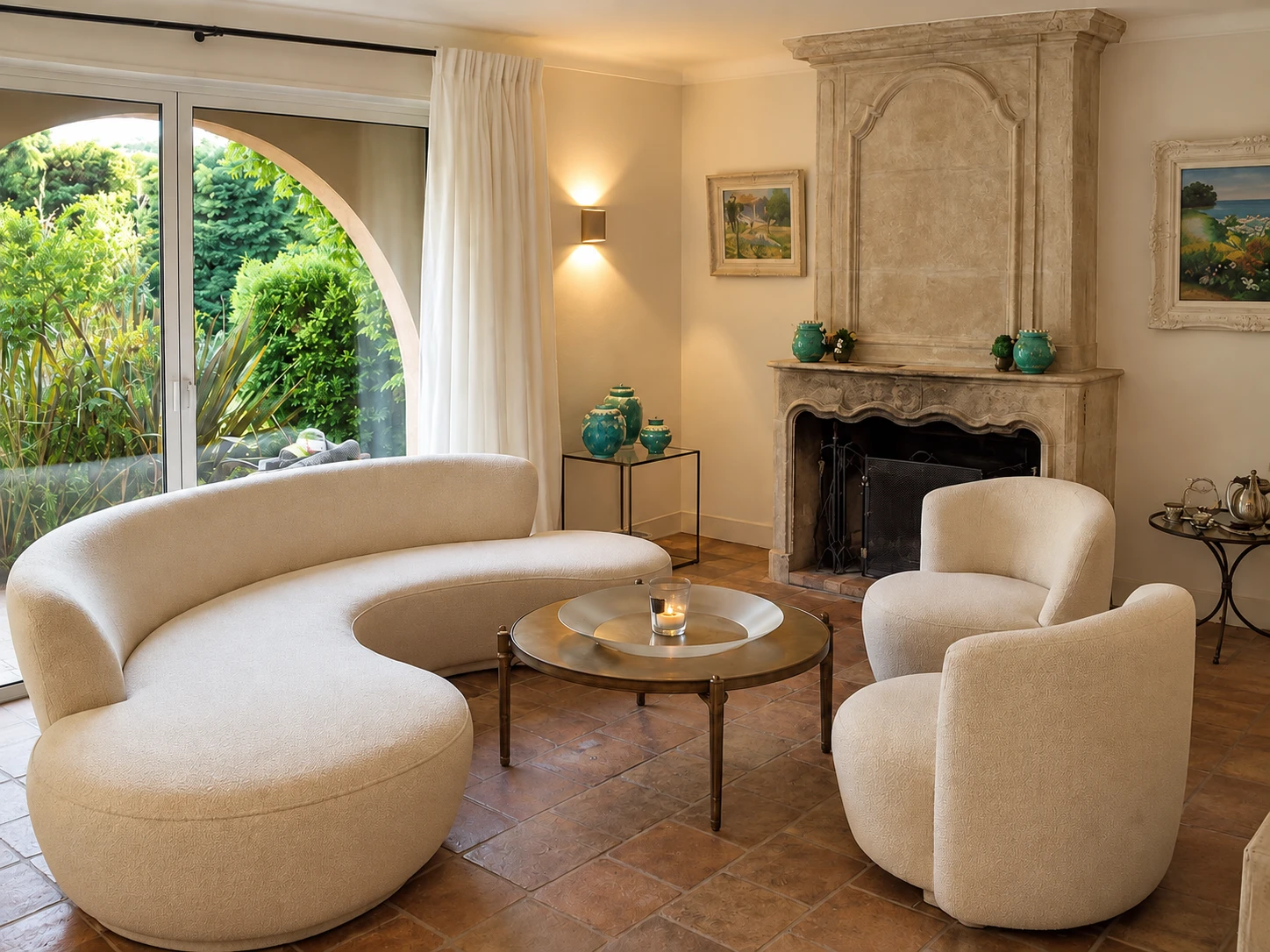 A living room with a curved cream sofa and two rounded armchairs around a brass table, beside a stone fireplace