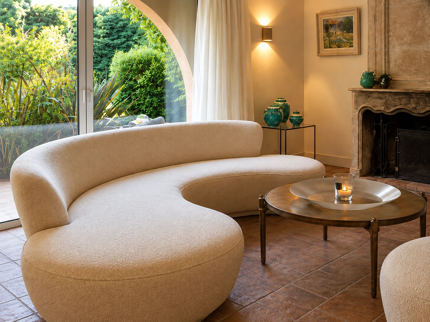 The curved cream sofa in front of the arched garden window, with a brass table and candle