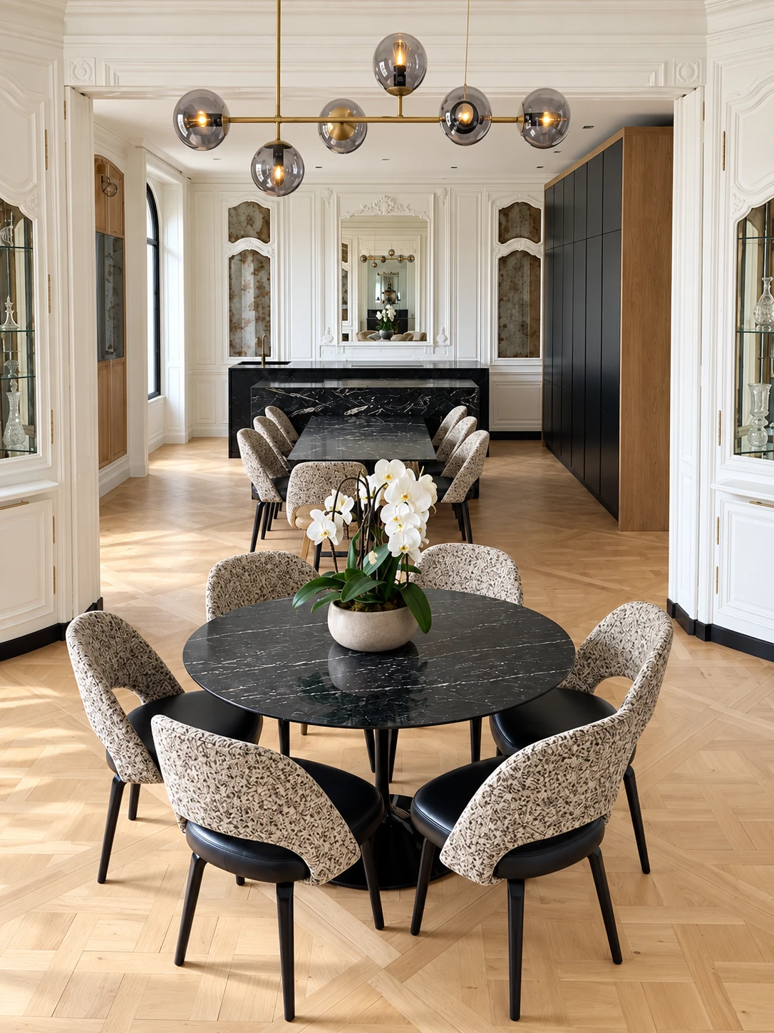 A round black marble dining table with patterned upholstered chairs and white orchids, under a brass and smoked-glass pendant