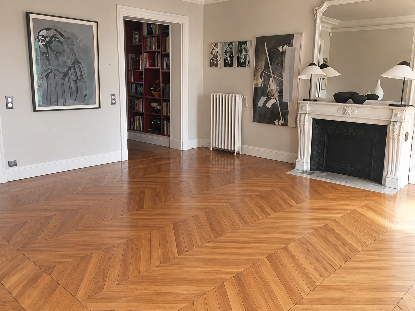 The same room before it was furnished: bare chevron parquet, the fireplace and the artworks on the walls