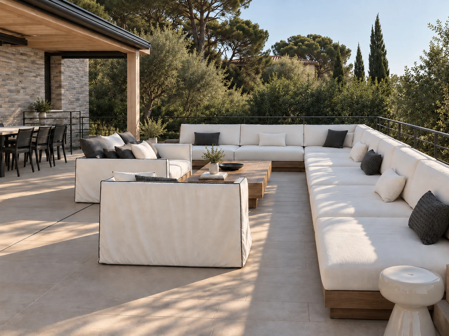 A terrace among olive trees and cypresses: a long built-in sofa on a timber plinth and two loose-covered sofas around a timber table